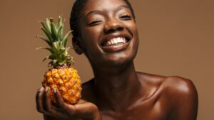 June femme souriante tenant un ananas dans ses mains dont est extrait la bromélaïne