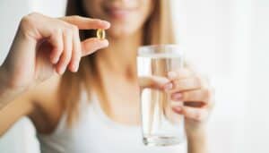 femme qui montre une gelule avec un verre d'eau